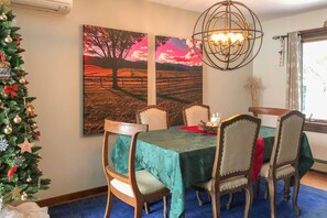 A dining area with a table set for six, surrounded by wooden chairs. There is a Christmas tree to the left, and two large landscape paintings on the wall. - Stowe Vacation Rental w/ Deck & Mountain Views! (Stowe)