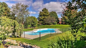 A backyard with a swimming pool, surrounded by a fence, trees, and a grassy lawn. - Stowe Vacation Rental w/ Deck & Mountain Views! (Stowe)