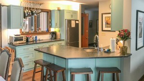 A kitchen with light blue cabinets, a stainless steel refrigerator, a built-in oven, and a bar stool area. - Stowe Vacation Rental w/ Deck & Mountain Views! (Stowe)