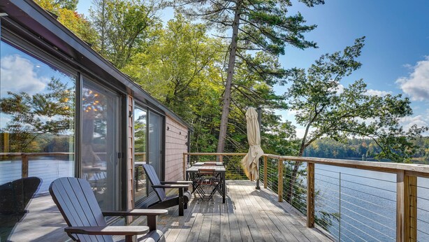 Terraza de madera con mobiliario exterior, con vistas a un lago rodeado de árboles.