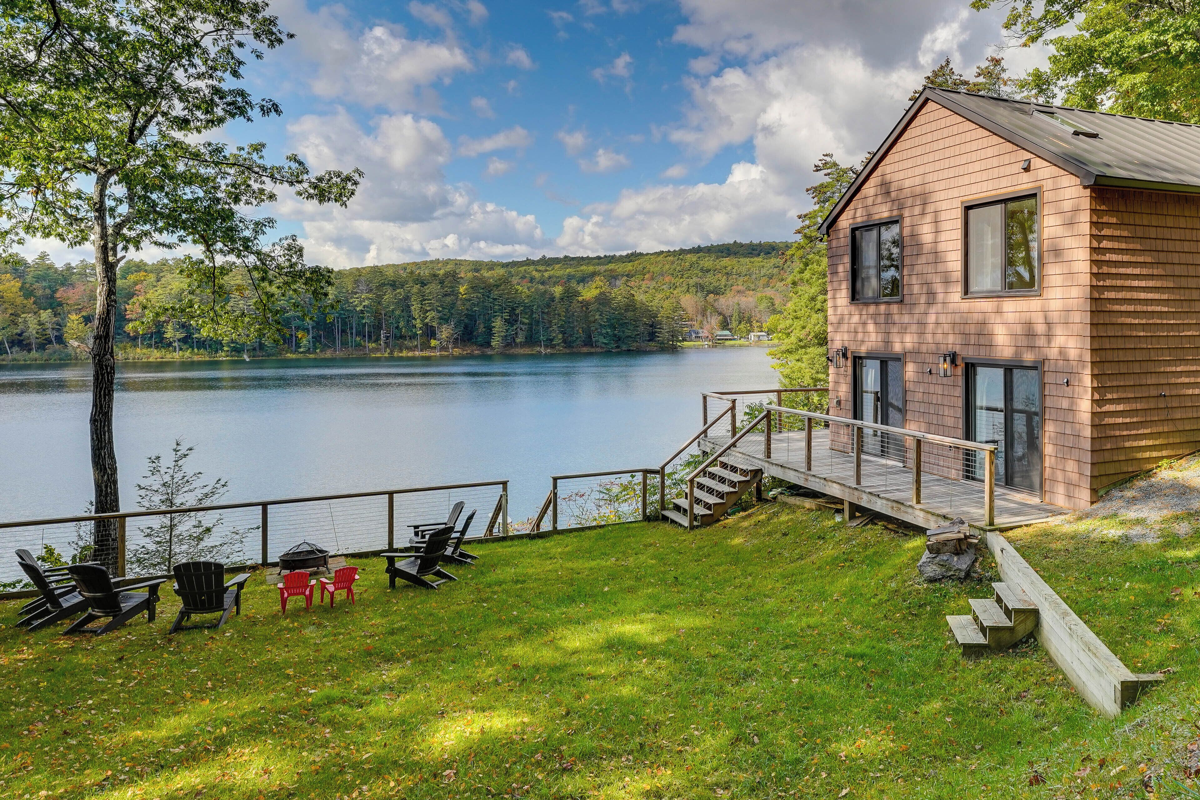 A cabin with a deck overlooking a lake, equipped with outdoor seating and a grill.