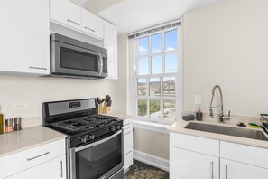 A modern kitchen with white cabinetry, a stainless steel stove, a microwave, and a window with a city view. - Cozy 1bd- Heart of Downtown Bham- Remote Workspace (Birmingham)