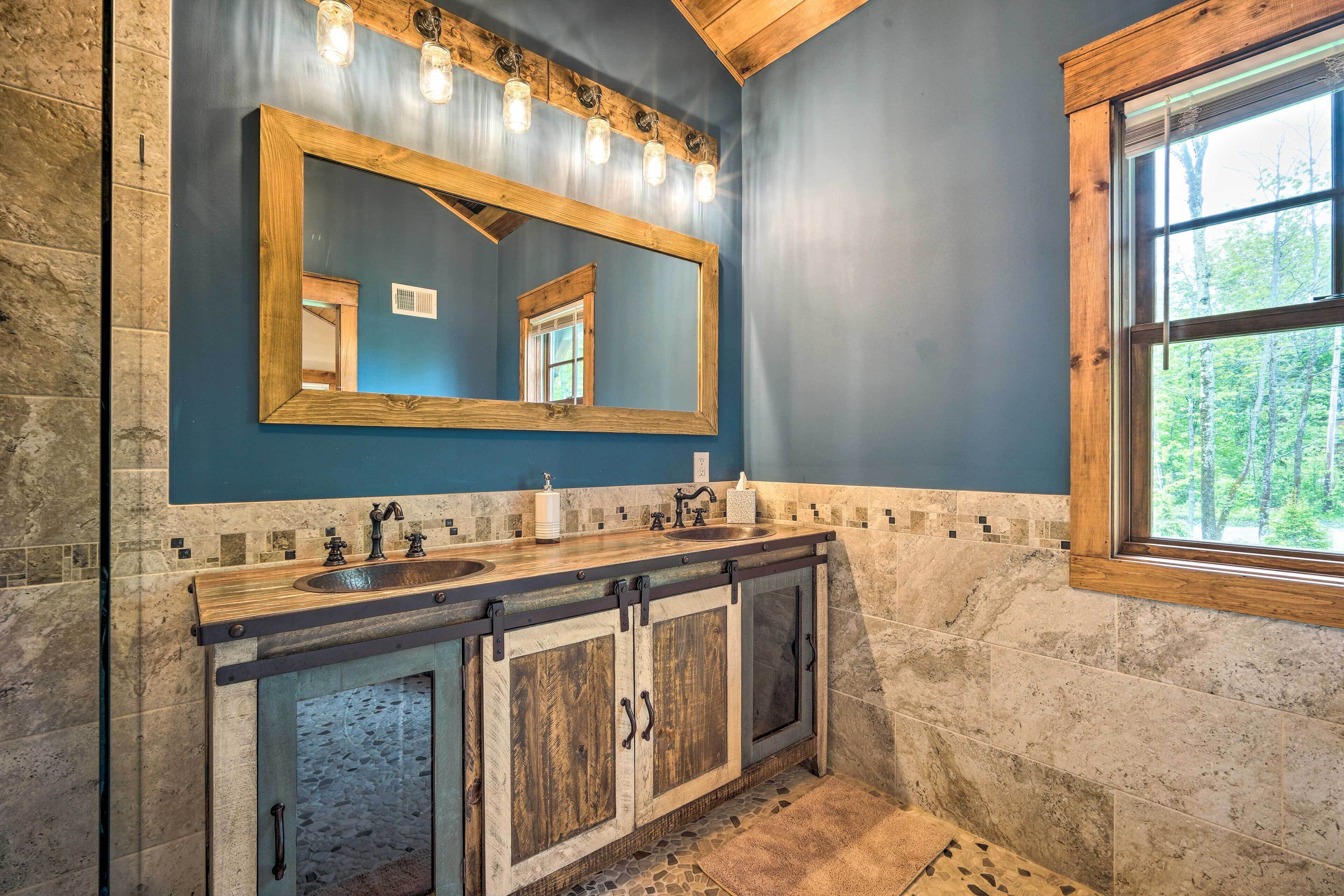A bathroom with a large mirror, wooden cabinets, a stone wall, and a window with a view of trees.