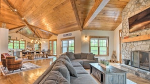 A spacious living room with a stone fireplace, wooden ceiling beams, and a large sectional sofa. - Elegant Mtn Chalet w/ Deck: 1 Mi to Mt Snow! (West Dover)