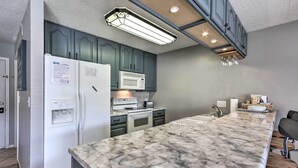 Una cocina con encimera de mármol, refrigerador, microondas y estufa.