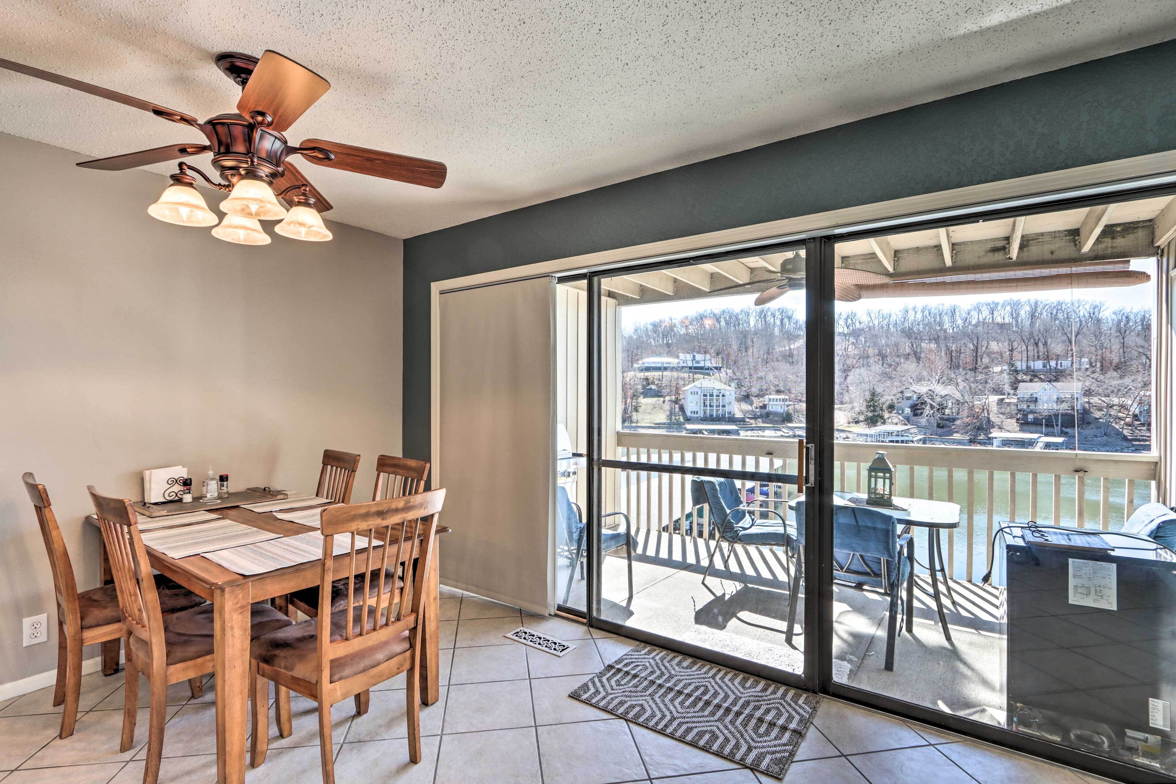 A dining area with a table and chairs, a ceiling fan, and a large sliding glass door leading to a balcony with a view of a residential area.