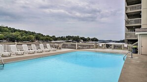 Una piscina con sillones de descanso y vistas a una colina arbolada.