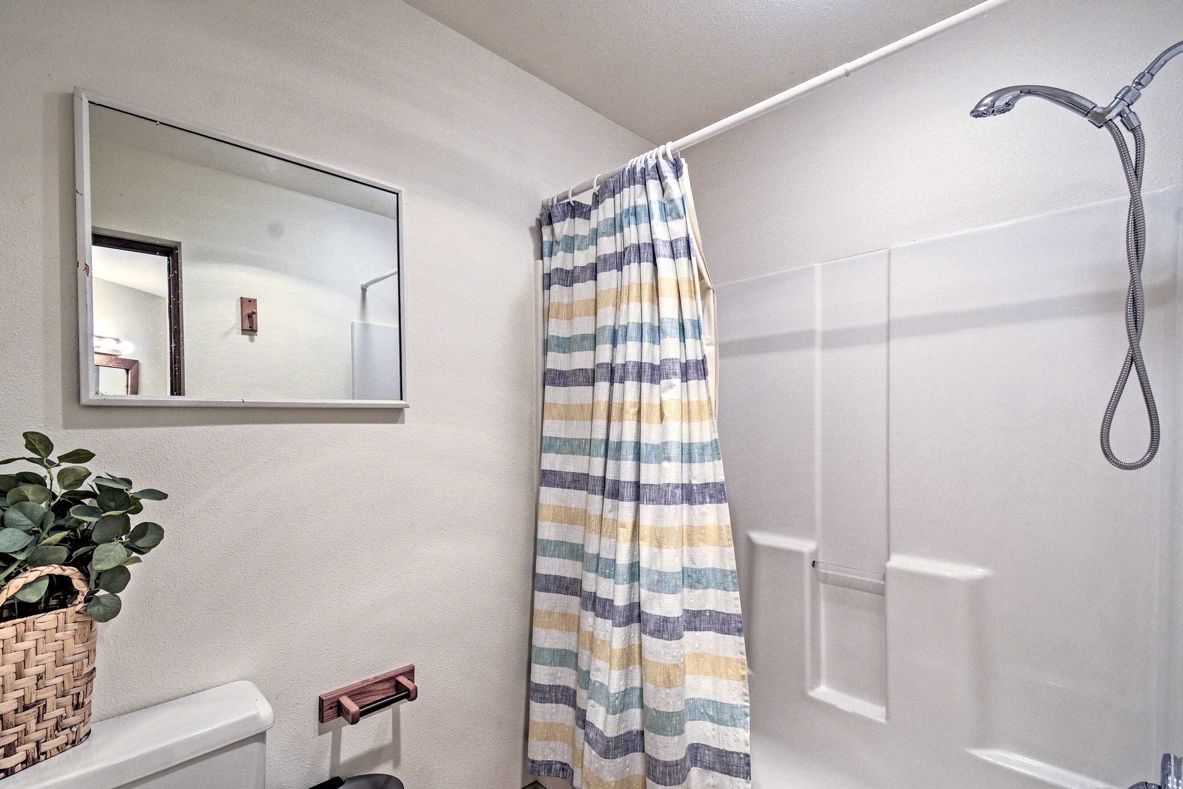 Un baño con cortina de ducha, un espejo, una planta en maceta y un perchero para toallas.