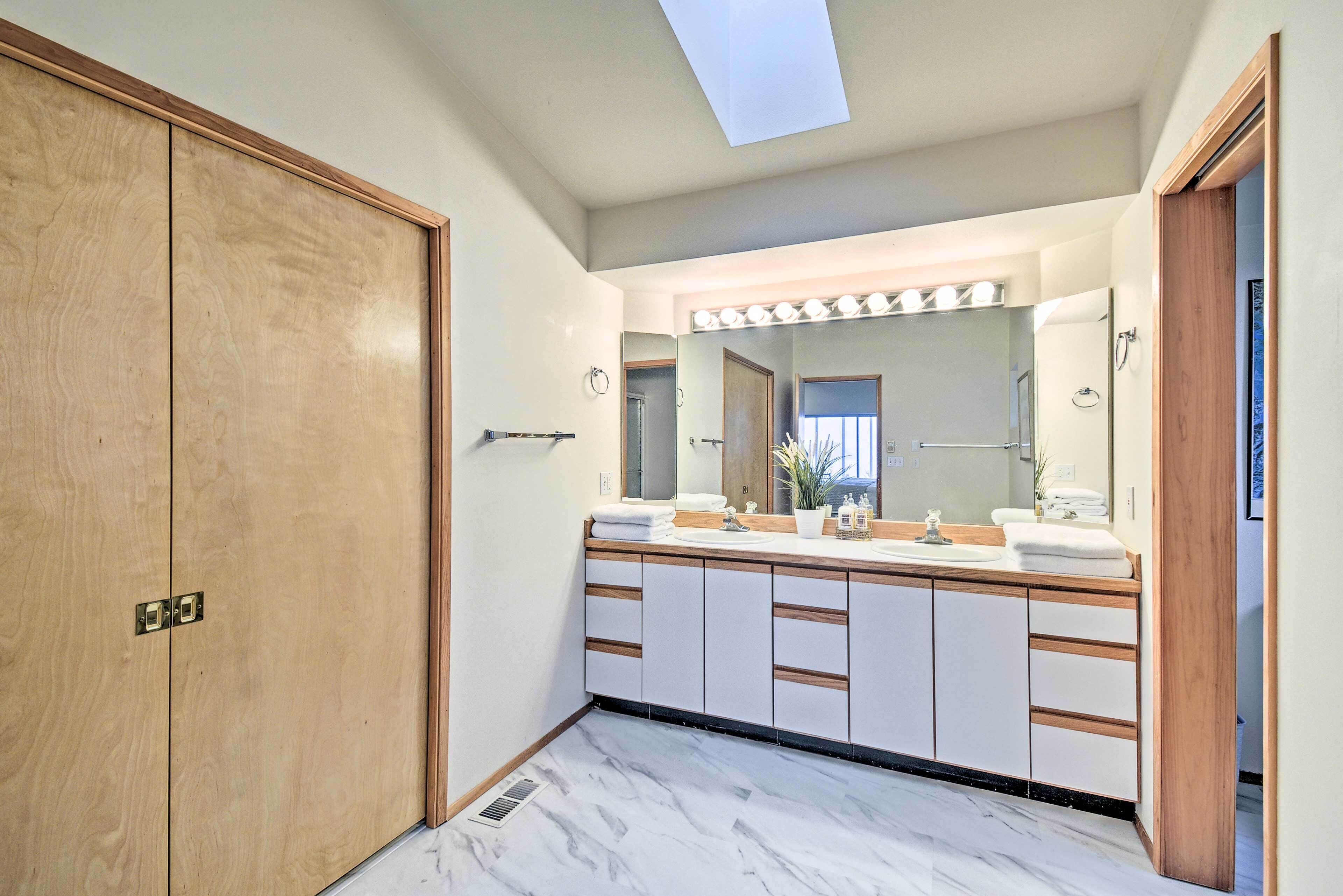 A bathroom with a wooden vanity, a large mirror, and a skylight.
