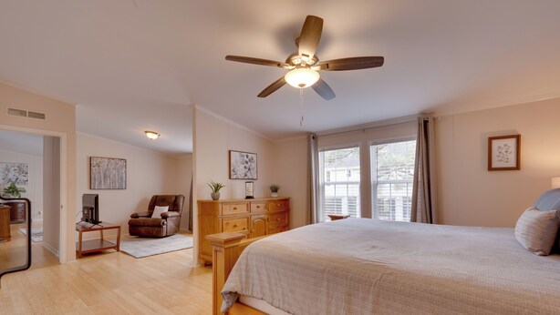 Une chambre à coucher avec un lit en bois, un ventilateur de plafond, une commode, une chaise et une fenêtre avec des rideaux.