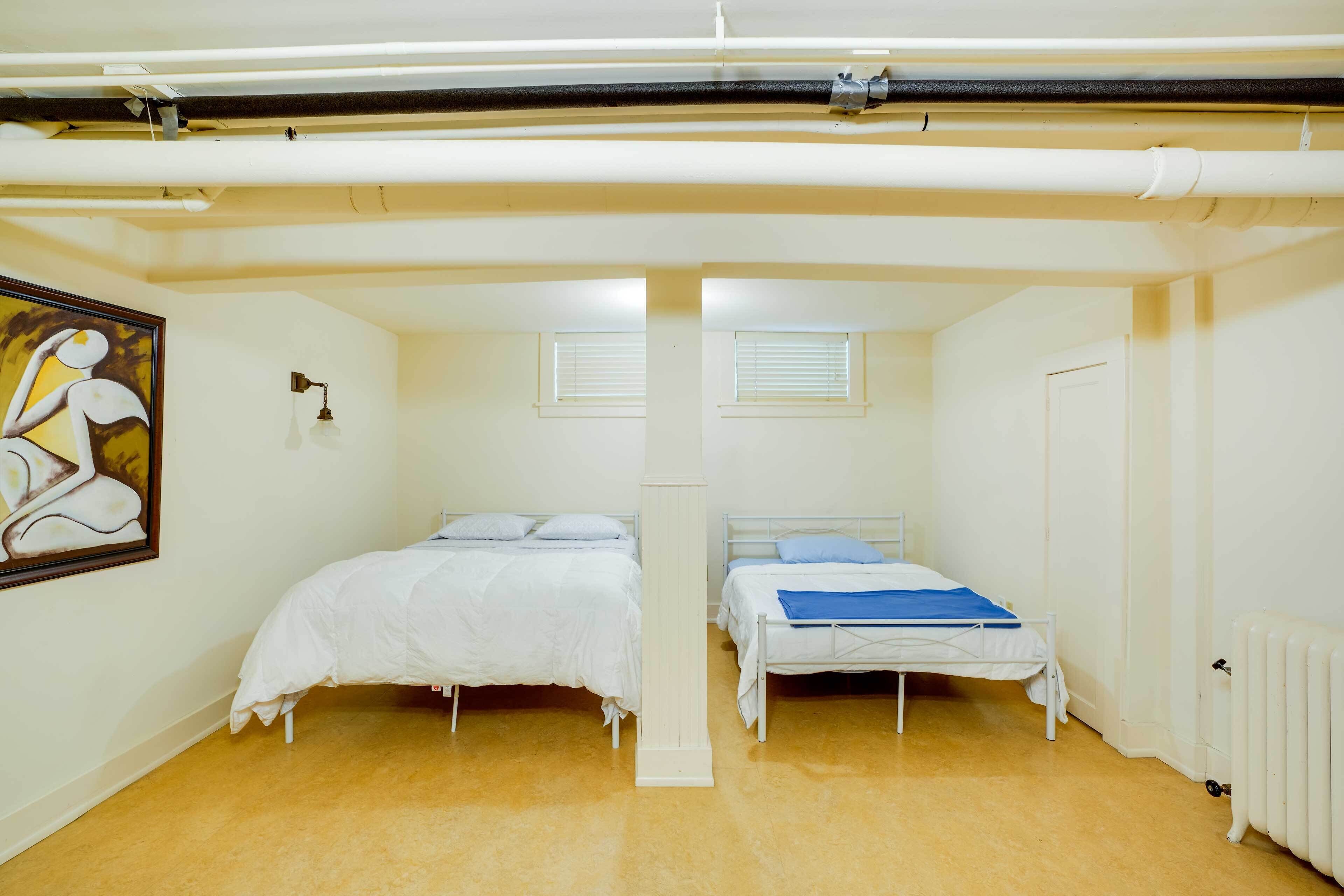 A room with two beds, a radiator, a painting, and a window with blinds.