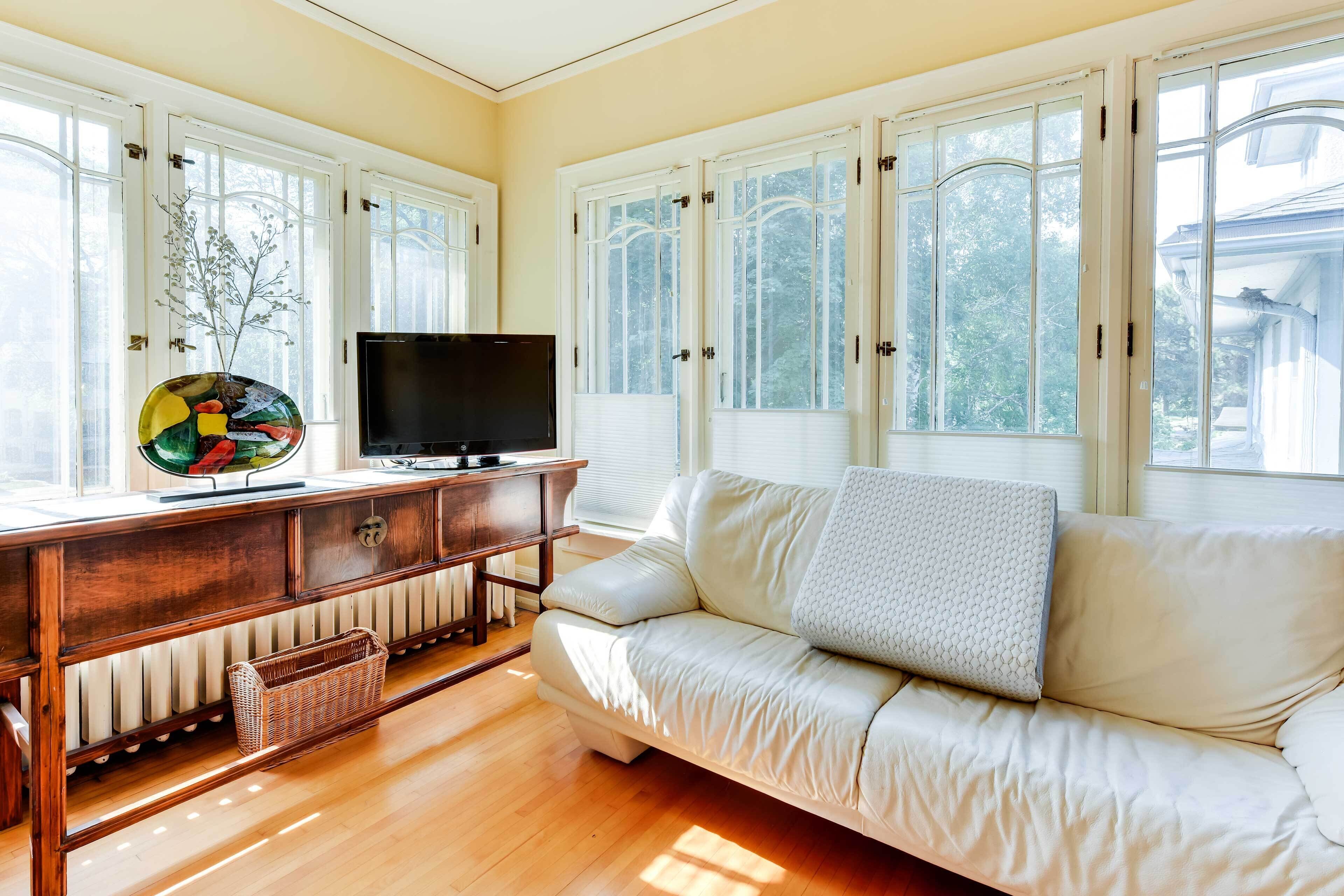A living room with a sofa, TV, wooden cabinet, and large windows.