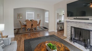 A living room with a fireplace, a dining area with chairs and a table, and a television mounted on the wall. - Near Churchill Downs: Pet Friendly, Fenced Yard! (Louisville)