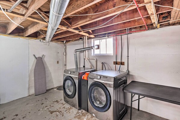 A laundry room with two stacked front-loading washing machines, a metal table, and exposed wooden beams.