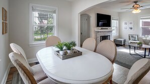 A dining area with a round table, chairs, and a tray of plants. There is a television mounted above a fireplace, and a ceiling fan is visible. - Near Churchill Downs: Pet Friendly, Fenced Yard! (Louisville)