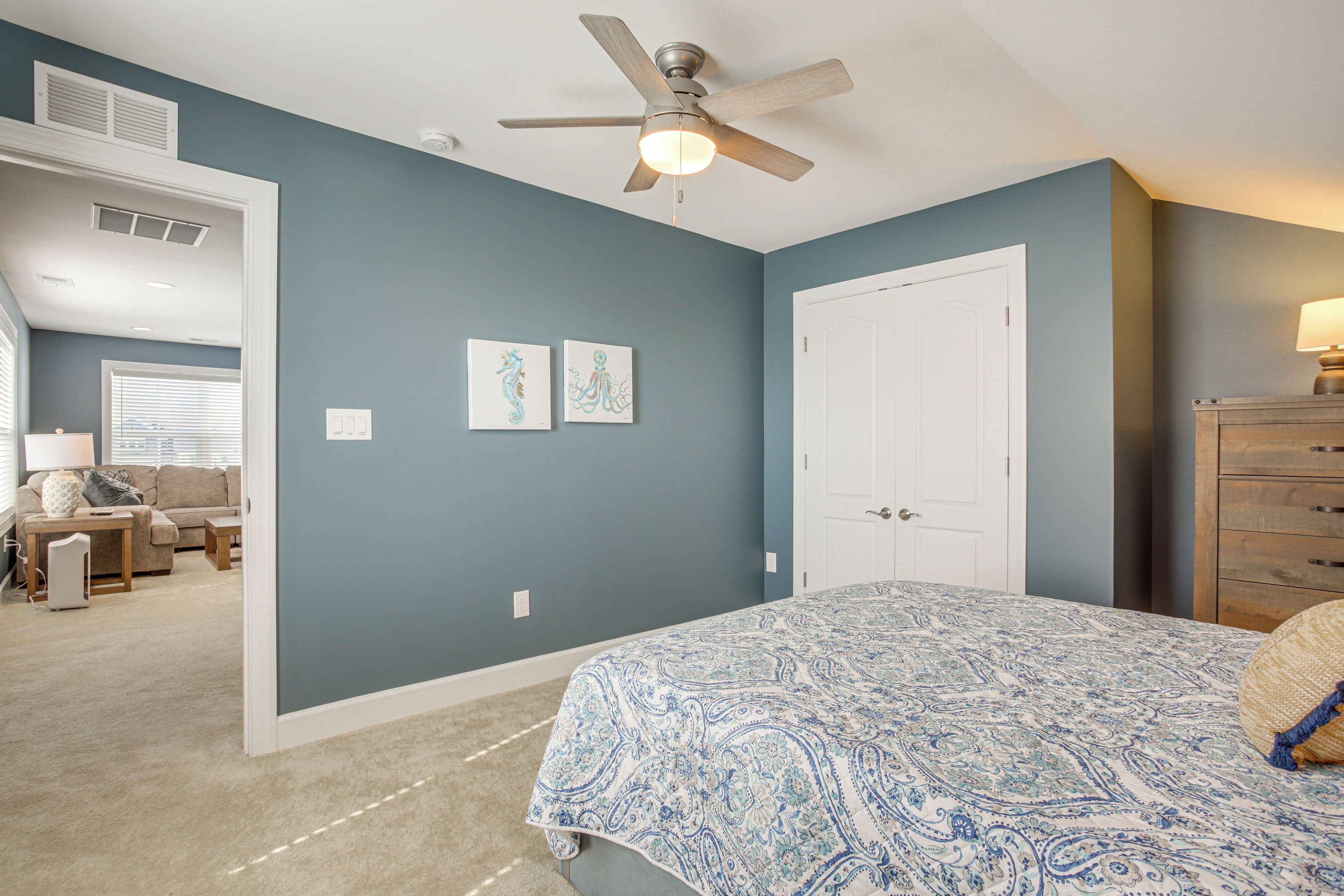 A bedroom with a bed, a ceiling fan, a door, and a dresser.