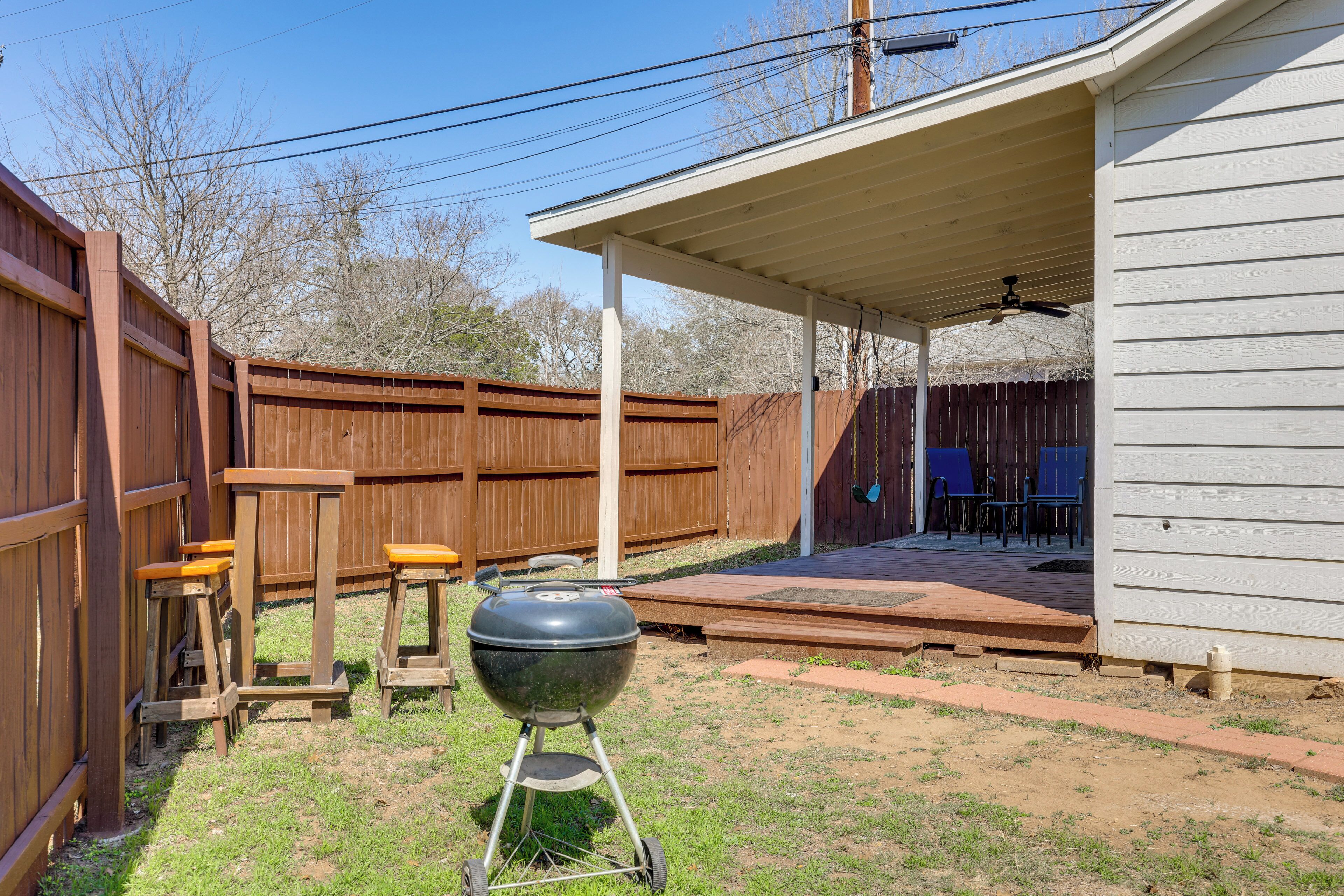 A backyard with a barbecue grill, wooden stools, and a covered patio area.