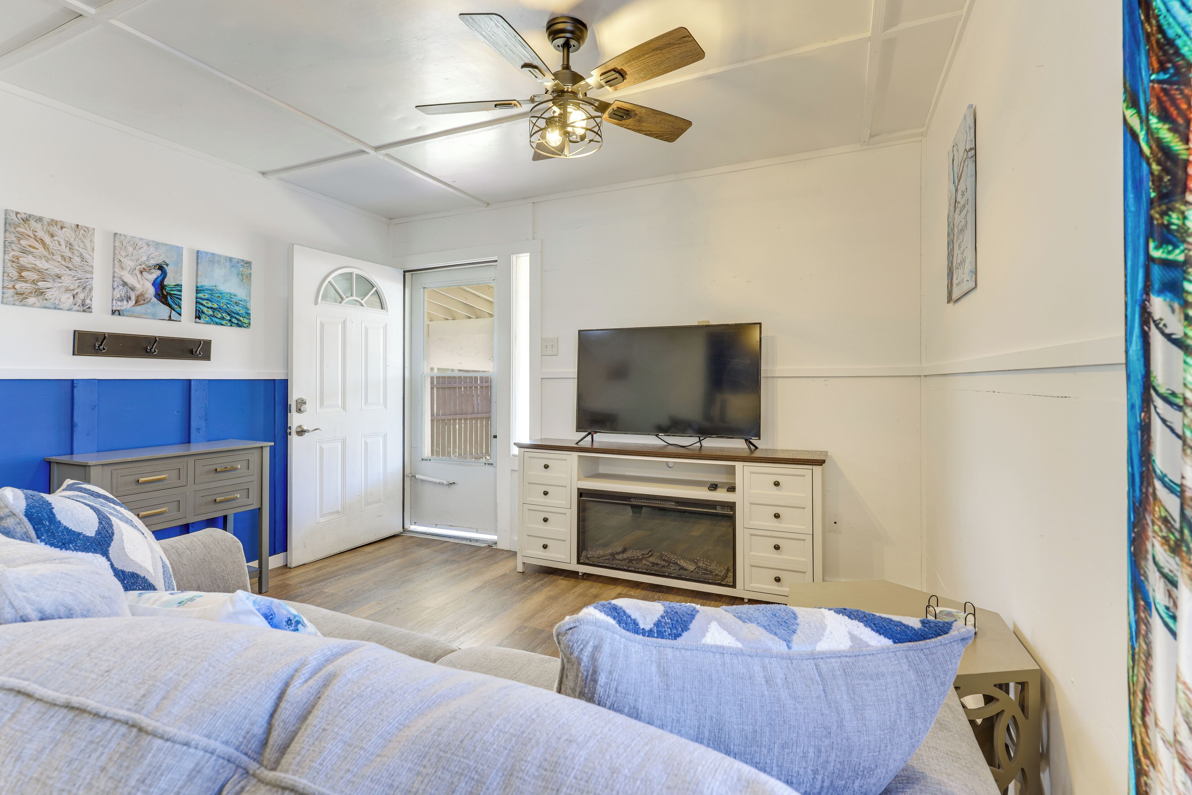 A bedroom with a bed, a TV, a ceiling fan, and a door leading to another room.