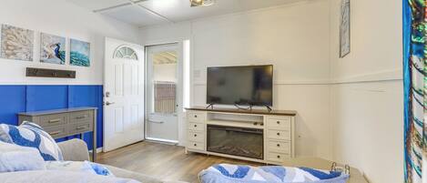 A bedroom with a bed, a TV, a ceiling fan, and a door leading to another room.