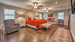 A spacious bedroom with a large bed, a chair, a bench, and two ceiling fans.