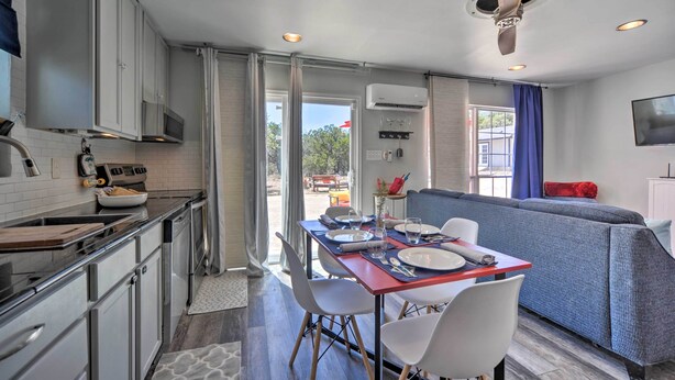 Una cocina moderna con armarios blancos, un comedor con una mesa roja y un sofá azul.