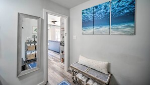 Un pasillo con un espejo, un banco con toallas y una obra de arte en la pared que representa olas del océano.