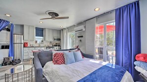 Un dormitorio moderno con una cama grande, un escritorio pequeño y una kitchenette al fondo.
