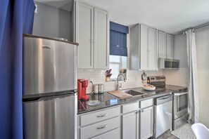 A modern kitchen with stainless steel appliances, white cabinets, and a blue window blind.