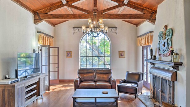 A spacious living room with a wooden ceiling, a large window, a fireplace, and leather furniture.