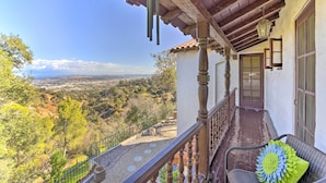 A balcony with a view of a valley, a wooden railing, and a bench with a flower cushion.