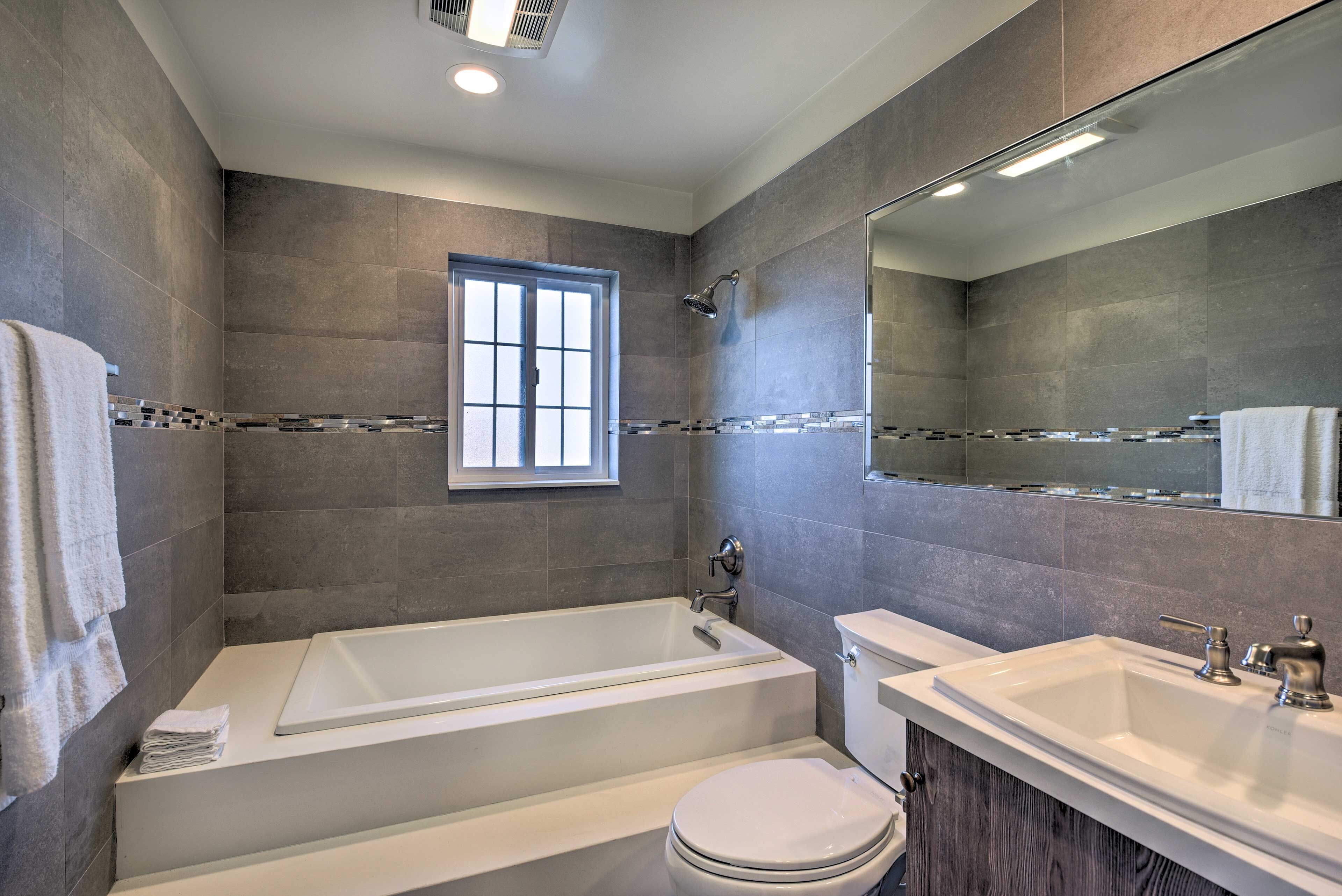 Ein modernes Badezimmer mit Badewanne, Toilette und Waschbecken, mit grauen Fliesen und einem großen Spiegel.