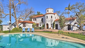 A white building with red-tiled roofs, a pool, and blue chairs.