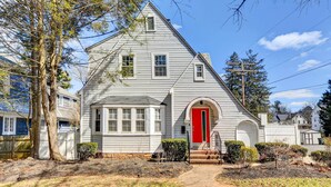 A two-story house with a red front door, a small porch, and a well-maintained lawn. - Updated Baltimore Home 8 Mi to Downtown! (Baltimore)