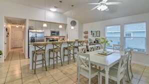 Una cocina moderna con una isla central, taburetes de bar y una mesa de comedor con sillas.