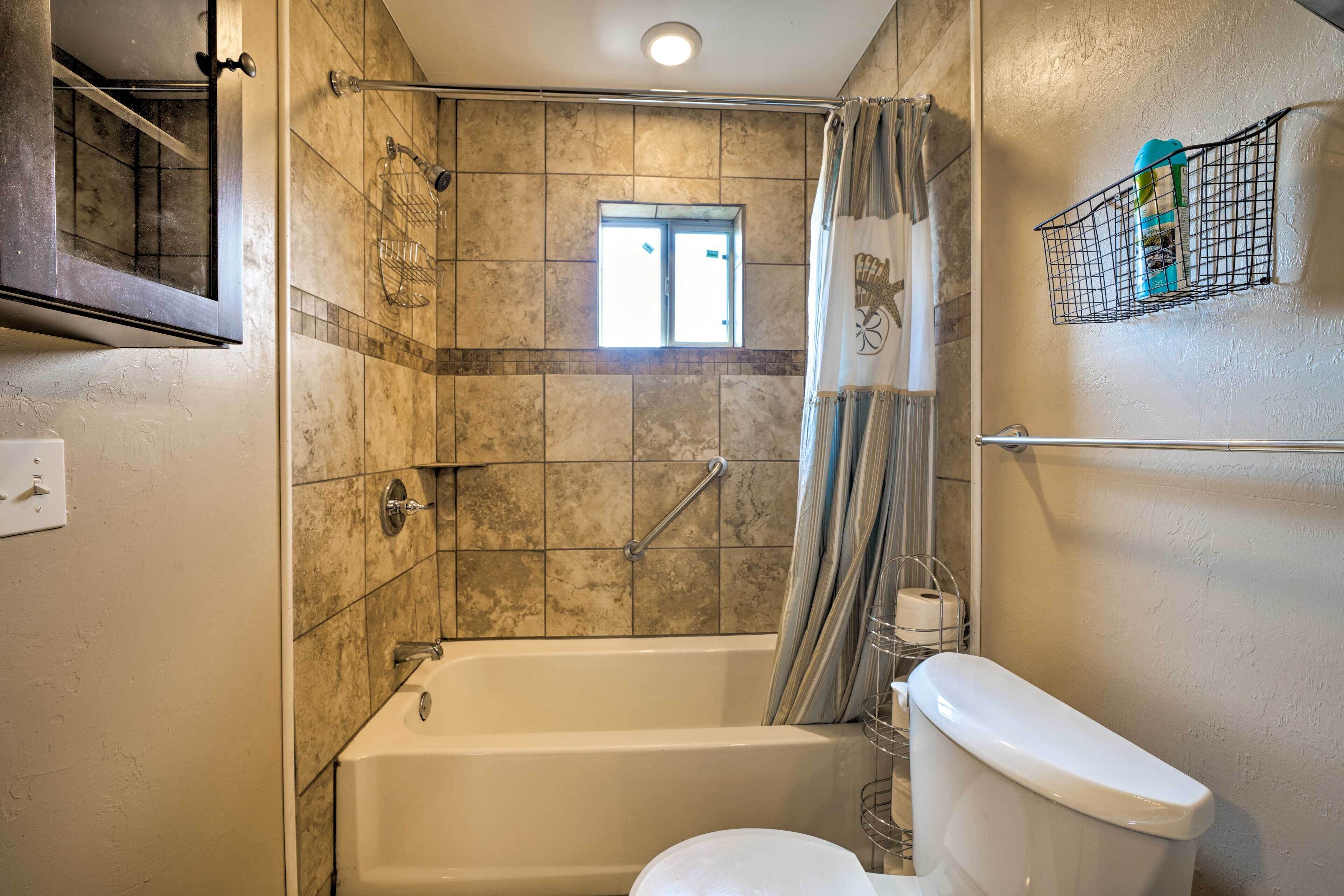 A bathroom with a bathtub, toilet, shower, and a window.