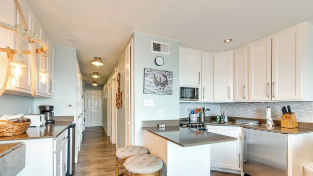 A modern kitchen with white cabinets, a stainless steel refrigerator, and a central island with stools. - Family Beach Retreat w/ Pool & Views in Galveston (Galveston)