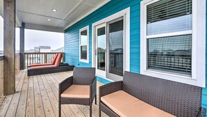 A covered deck with wicker furniture and a view of the ocean.