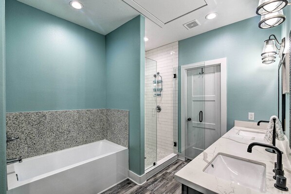 A modern bathroom with a bathtub, a glass-enclosed shower, and two sinks with marble countertops.