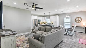 A modern living room with a sectional sofa, a coffee table, and a rug. There is a dining area with a table and chairs, and a kitchen in the background.