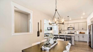 A modern kitchen with white cabinets, a wooden dining table, and a chandelier. - Walk to Parks! Billings Gem w/ Soaking Tub (Billings)