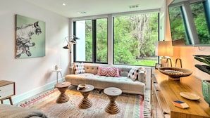 Un salon moderne avec une grande fenêtre, un canapé, deux petites tables en bois et un lampadaire.