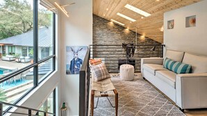 Un salon moderne avec un canapé blanc, un banc agrémenté de coussins, une grande fenêtre et une vue sur une piscine et un espace extérieur.