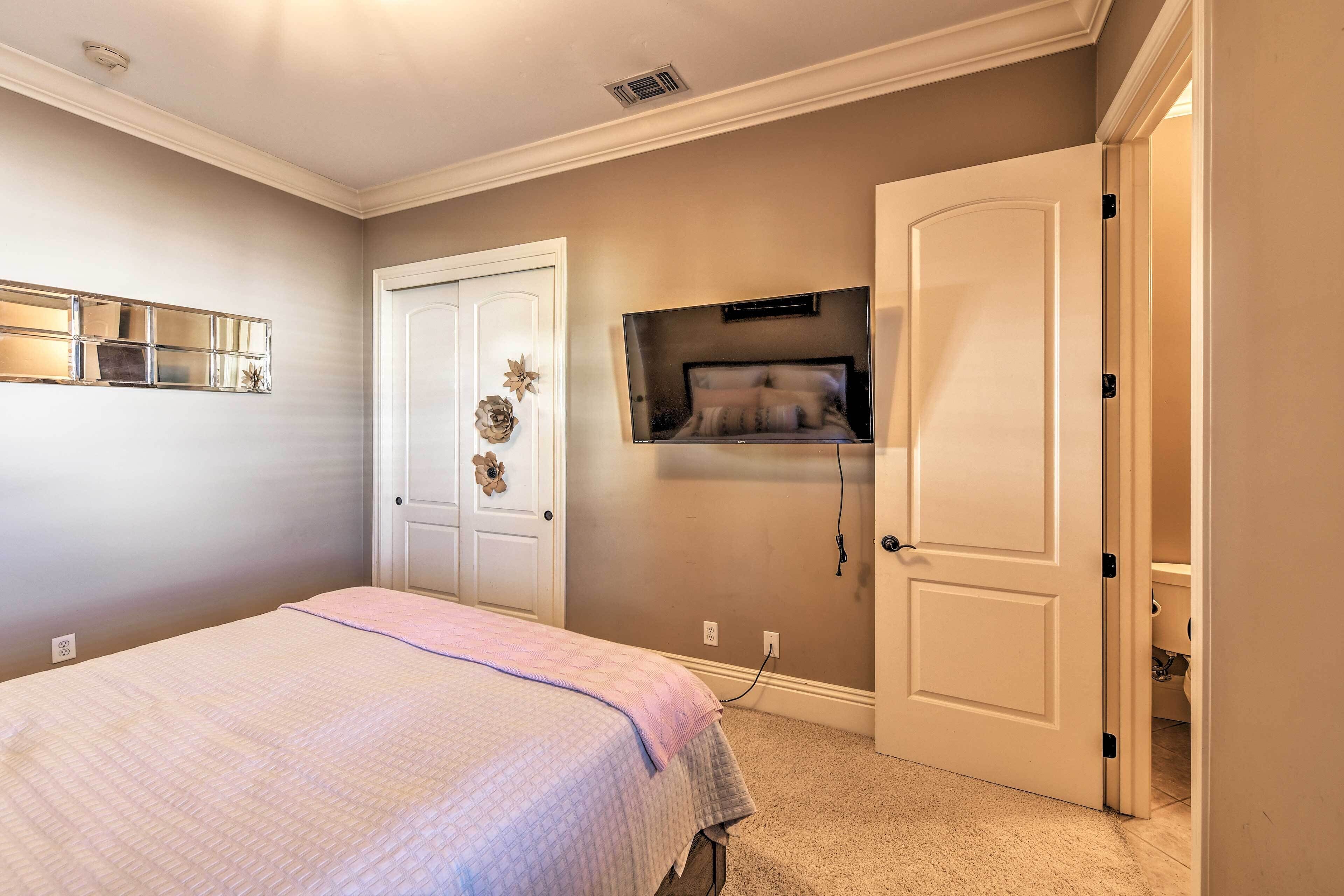 A bedroom with a bed, a wall-mounted TV, a door, and a small shelf.