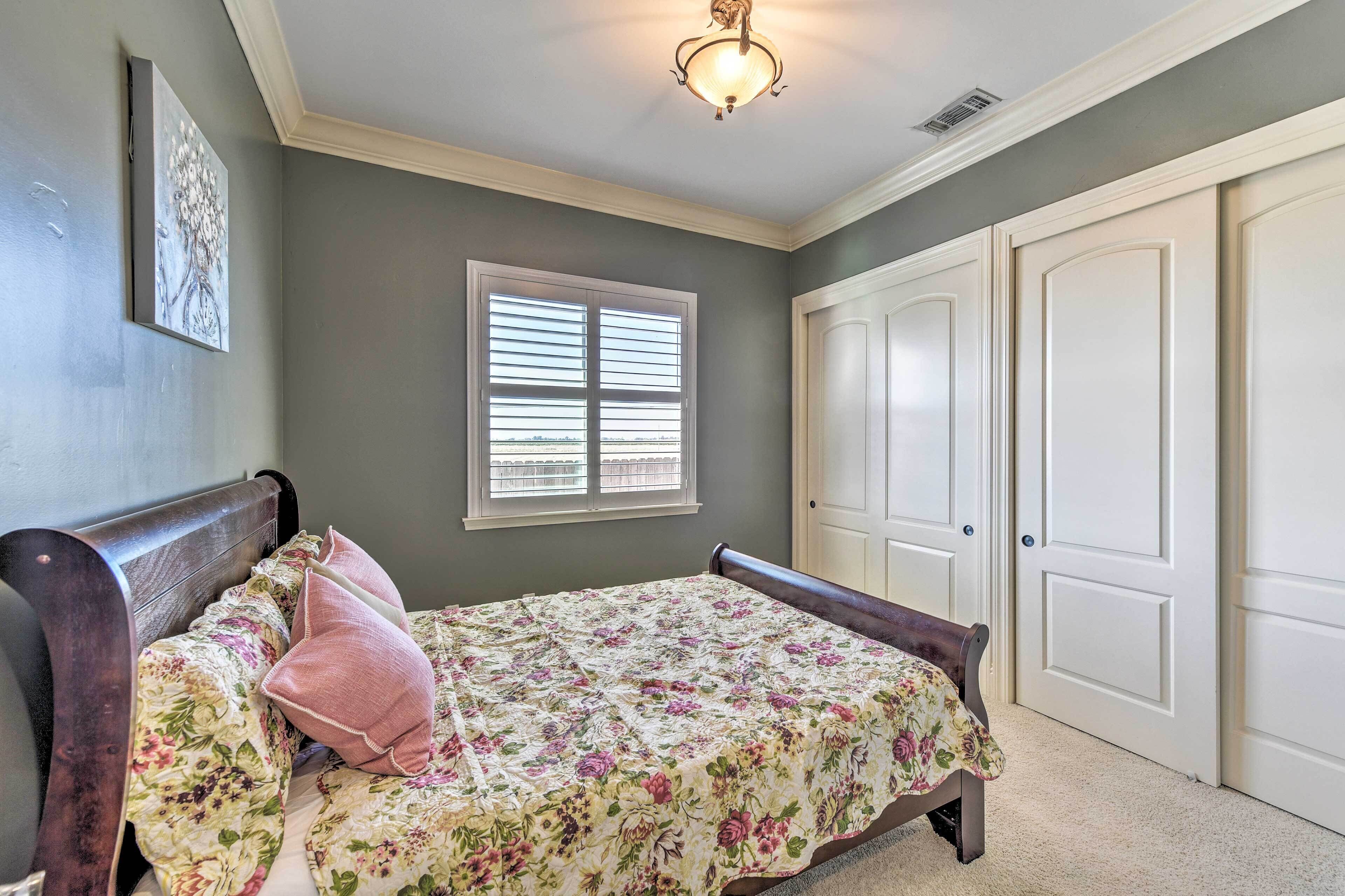 A bedroom with a bed, a window with blinds, a door, and a ceiling light fixture.