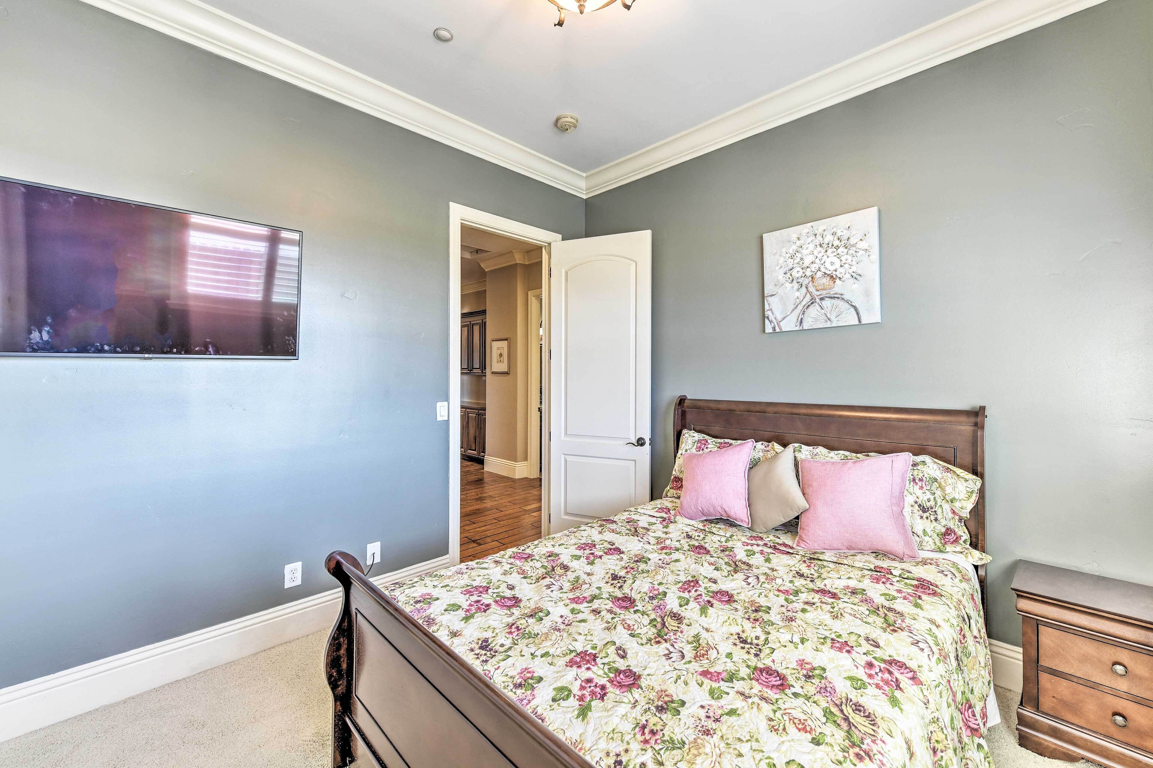 A bedroom with a bed, a nightstand, a wall-mounted TV, and a door leading to another room.