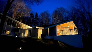 Una casa moderna con ventanas grandes y un balcón, rodeada de árboles.