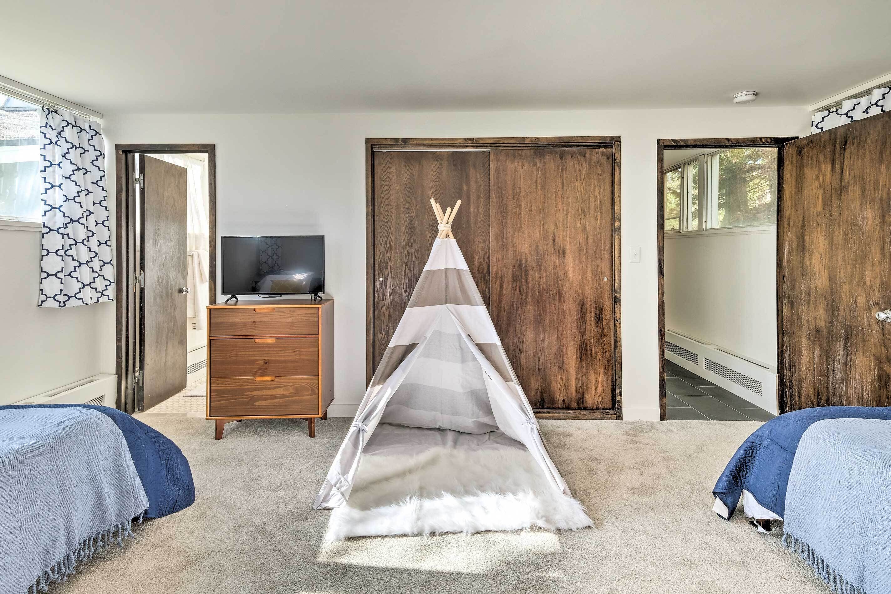 A bedroom with a large wardrobe, a television, a bed with a blue blanket, and a teepee tent.