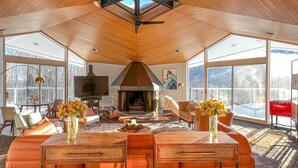 Amplia sala de estar con techo de madera, chimenea y vista al exterior.