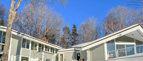 A modern building with large windows and a covered entrance, surrounded by snow and leafless trees.