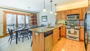 A kitchen with wooden cabinets, a stainless steel refrigerator, a microwave, an oven, and a dishwasher. There is a dining table with chairs and a chandelier. - Inviting Ski-in/ski-out Condo at Jay Peak Resort! (North Troy)